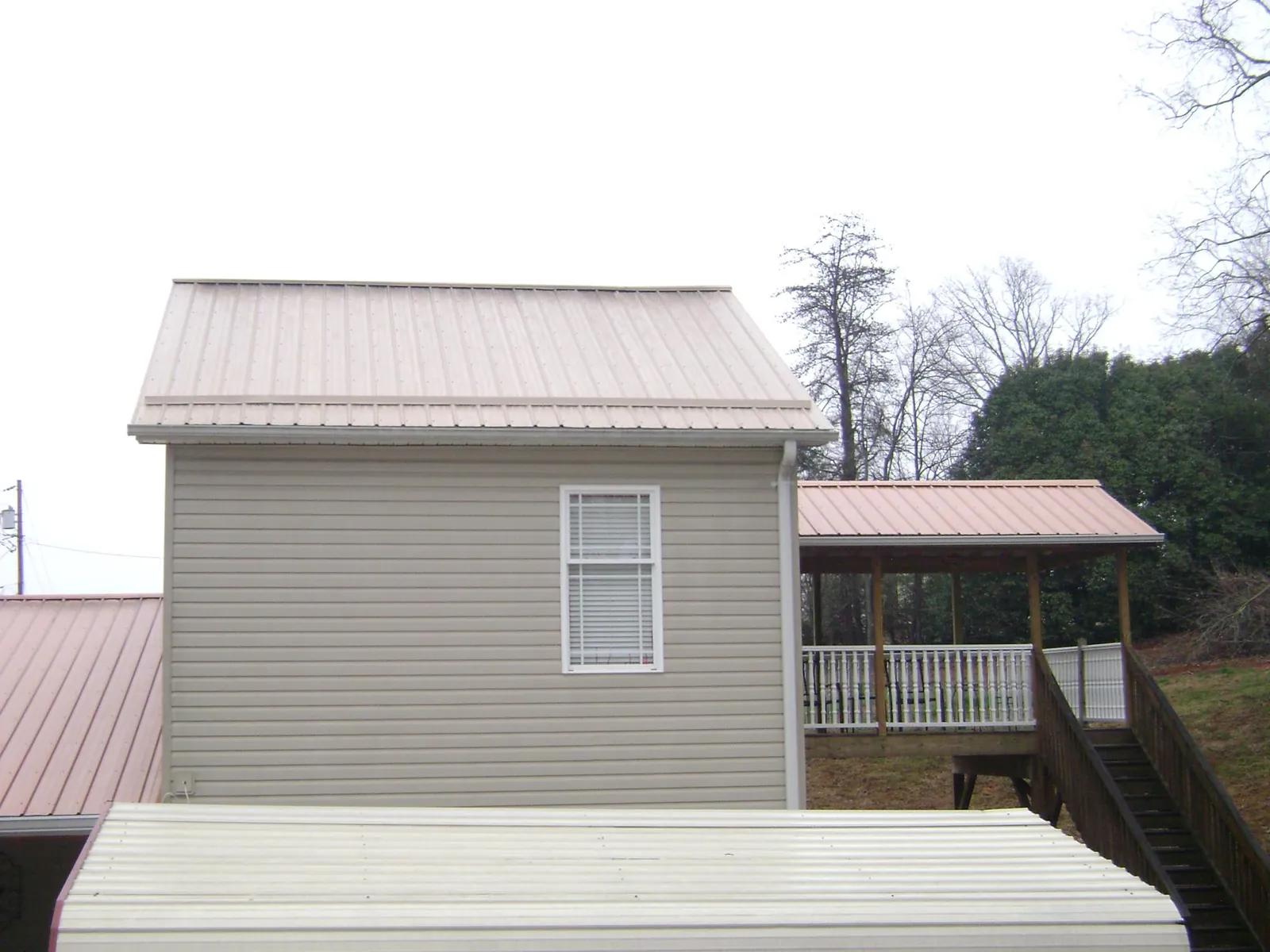 Tan metal roofs on a two story addition and attached porch, from a Roof Replacement job in Raleigh